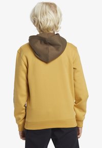 Huvtröja i senapsgul med brun huva. Har en avslappnad passform, ribbade ärmar och grafik på ryggen. Material i bomullsblandning.