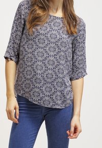 Blusa navy con motivo floreale, maniche corte e orlo leggermente curvo. Realizzata in tessuto leggero con una consistenza liscia.