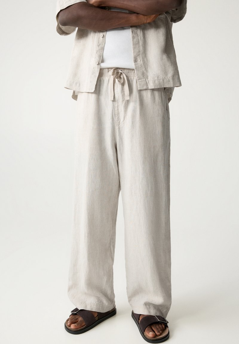 Vaaleanbeige pellavapaitapusero, jossa on vastaavat löysät pellavahousut. Rentoa leikkausta, joustava vyötärönauha ja soljella varustetut litteät sandaalit.