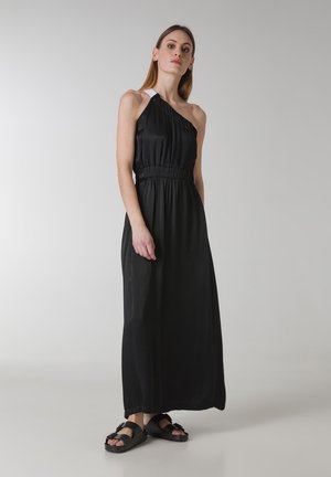 Lang sort kjole med en skulderrem, samlet talje og flydende skirt. Materialet er glat med en let glans; parret med sorte sandaler.
