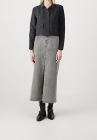 Czarna krótka kurtka z dwoma przednimi kieszeniami, zestawiona z szarą długą dżinsową spódnicą z przednim rozcięciem. Całość dopełniają czarne kozaki za kolano.