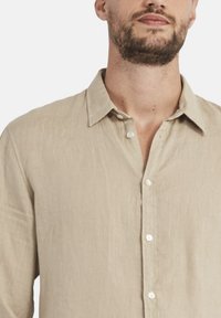 Camicia di lino beige con colletto a polo, dotata di bottoni bianchi, texture visibile e vestibilità comoda.