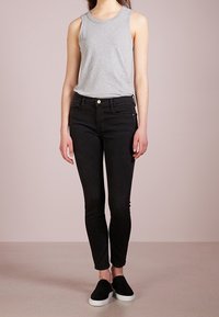 Haut sans manches gris, jean noir slim, et chaussures noires à enfiler. Design simple, tissu doux, avec une coupe classique.