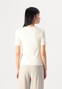 Geribbelde witte, kort mouwige top met een ronde halslijn, aansluitend ontwerp en een gladde textuur. Gemaakt met een lichte broek.