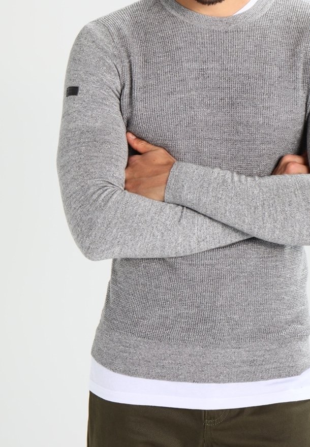 Maglione grigio a maniche lunghe in maglia con una finitura testurizzata, collo rotondo e una vita liscia, dotato di un piccolo etichetta nera sul braccio sinistro.