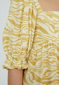 Geel en witte jurk met een zebra-streep patroon, pofmouwen met een gathered manchetten, en een getailleerd lijfje dat overgaat in een uitlopende rok.