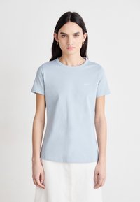 Light blue cotton t-shirt with short sleeves and a round neckline. Features minimalistic white embroidered detail on the chest.