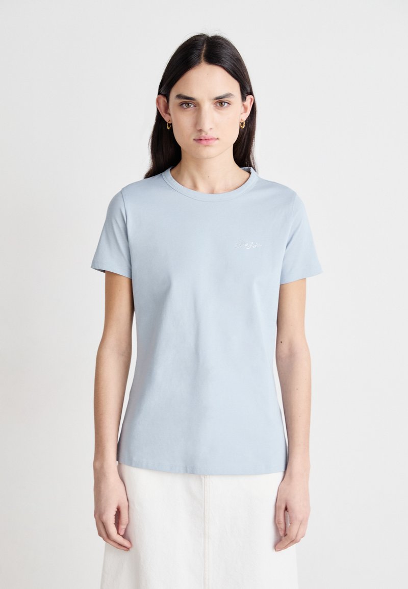 Light blue cotton t-shirt with short sleeves and a round neckline. Features minimalistic white embroidered detail on the chest.