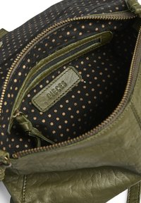Intérieur d'un sac en cuir vert montrant une doublure en tissu noir avec des pois dorés, comportant une poche zippée et une étiquette "PIECES".