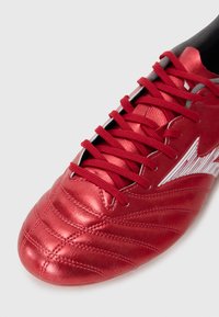 Rode voetbalschoen met een bovenwerk van textuurleer, voorzien van een vetersluiting en een witte accentstreep langs de zijkant.