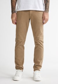 Chinos de algodón beige con un corte ajustado y una textura suave. Acompañados de zapatillas blancas. Líneas limpias y detalles de costura mínimos.