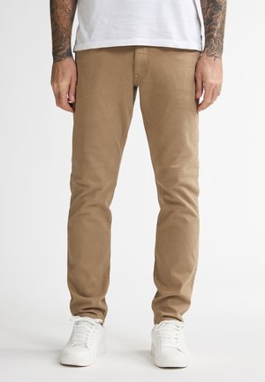 Chinos de algodón beige con un corte ajustado y una textura suave. Acompañados de zapatillas blancas. Líneas limpias y detalles de costura mínimos.