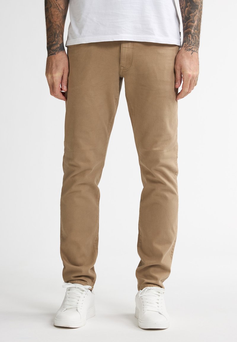 Chinos de algodón beige con un corte ajustado y una textura suave. Acompañados de zapatillas blancas. Líneas limpias y detalles de costura mínimos.