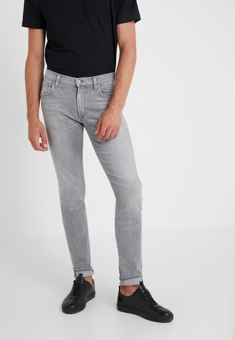 Šedé slim-fit džíny s jemně vybledlou texturou, s pěti kapsami a zapínáním na knoflík, v kombinaci s černými teniskami.