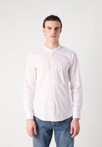 White long-sleeve shirt with a band collar, featuring front buttons and a smooth texture, paired with blue denim jeans.