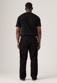 Black short-sleeve t-shirt paired with black jeans, featuring a straight cut and visible back pockets. Simple design with no prominent patterns.