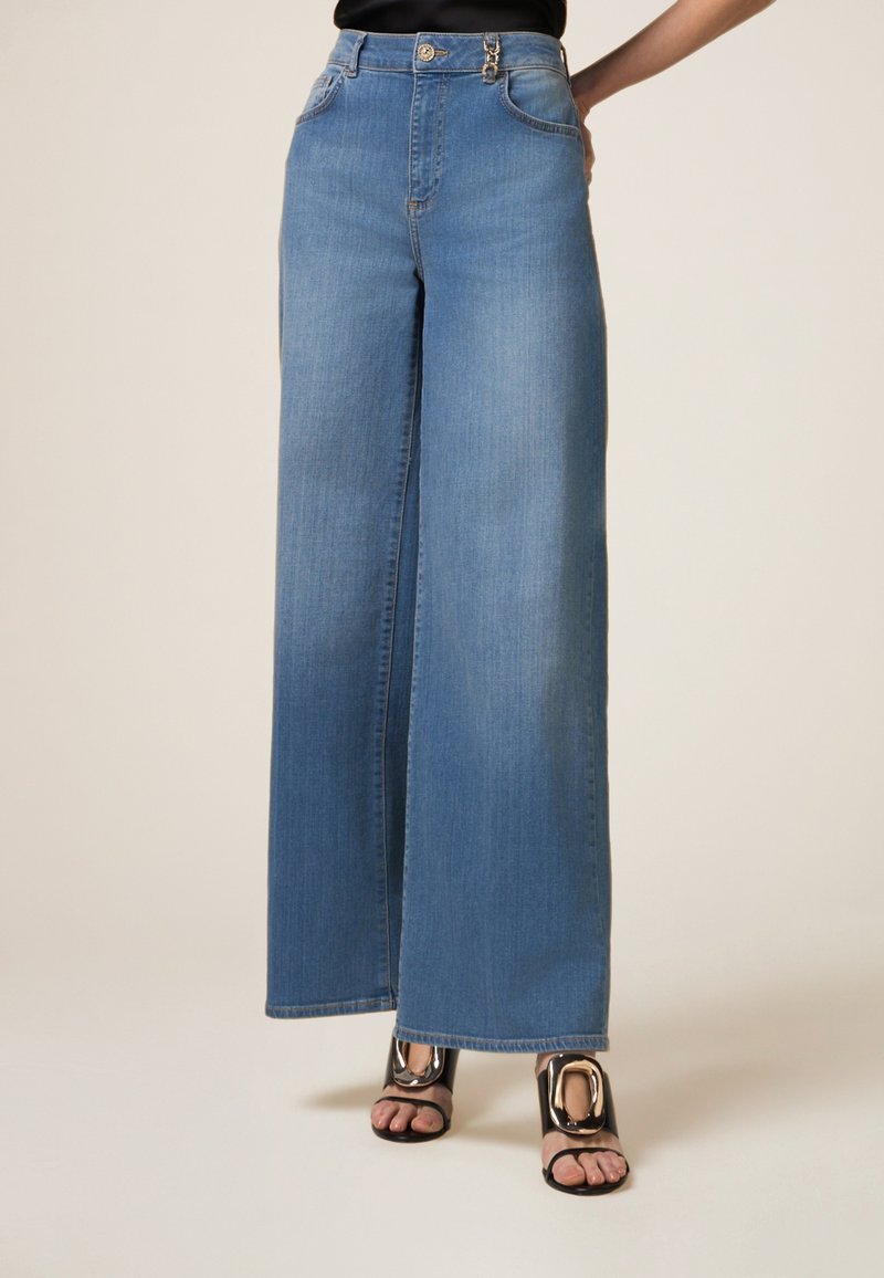Jeans a gamba larga di colore azzurro chiaro, realizzati in denim, con vita alta, due tasche frontali e un bottone argento in evidenza.