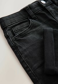 Jean en denim noir avec un design classique à cinq poches, passants pour ceinture et fermeture par bouton. Le tissu présente une texture lisse et un léger éclat.