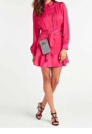 Robe rose vif à manches longues, col à boutons et taille nouée. Un petit sac noir et blanc à carreaux avec une bandoulière en chaîne complète le look.