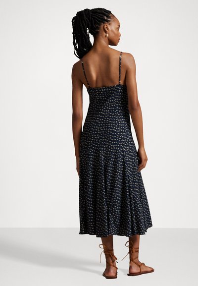 Navy blue, floral midi dress with thin straps and a fitted bodice, flowing skirt, and slight flounce. Worn with tan lace-up sandals.