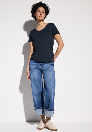 T-shirt blu navy a maniche corte, jeans blu con risvolto, e sneakers beige. Stile semplice e casual con una vestibilità rilassata. Tessuto dalla finitura morbida.