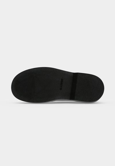 Semelle de chaussure plate noire avec une surface texturée et le nom de la marque "SANDRO" embossé au centre.