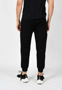 Sorte sweatpants med en tætsiddende pasform, lavet af et blødt stof. Har ribbede afslutninger og baglommer. Bæres med sorte og hvide sneakers.