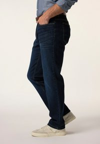 Mörkblå denimjeans med rak passform, med fem fickor, synlig sömnad och bärs med vita sneakers.
