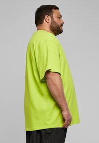T-shirt di un vivace verde lime in tessuto di cotone, con una vestibilità comoda e maniche corte, mostrata di lato su uno sfondo neutro.