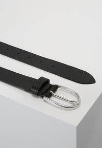 Ceinture en cuir noir avec une surface texturée, dotée d'une boucle à double ardillon en métal argenté et de plusieurs trous d'ajustement le long de la sangle.