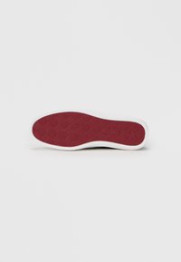 Semelle de chaussure en caoutchouc blanc avec un dessous rouge texturé arborant un motif en losanges pour l'adhérence. Bordure lisse autour des bords.