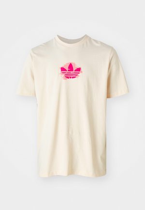 Kremfarvet T-shirt med korte ærmer og et pink, penselstrøgstil Adidas trefoil-logo centreret på brystet mod en hvid baggrund.