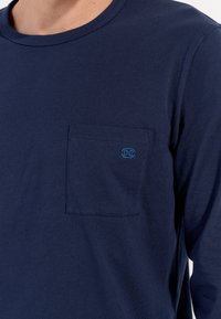 Marineblaue Langarm-T-Shirt aus Baumwolle mit Rundhalsausschnitt und einer Brusttasche, die mit einem blauen Logo versehen ist. Glatte Textur, lässiges Design.