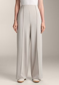 Ljusgrå högmidjade byxor med vida ben, försedda med framfickor och en slät yta. Materialet verkar mjukt och faller välsorterat.