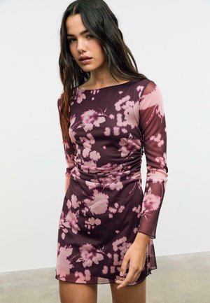 Robe mini florale en violet foncé et rose, avec des manches longues, une silhouette ajustée, des fronces à la taille et une texture transparente.
