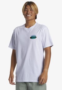 Camiseta de algodón blanco con un logotipo ovalado azul y verde que lleva la palabra "Gunslinger" arriba. Mangas cortas y corte relajado. Sin patrones.