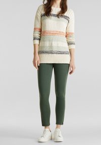 Pull en tricot crème avec des rayures multicolores ; associé à un pantalon vert ajusté et des baskets blanches. Tenue décontractée avec des textures contrastées.