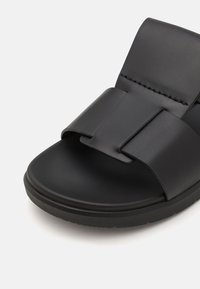 Svart slide sandal med en jevn matt finish, bred stropp og flat såle. Kjennetegnes av sitt minimalistiske design og rene linjer.