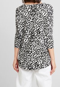 Černobílé tričko s dynamickým abstraktním vzorem, tříčtvrteční rukávy, kulatý výstřih a volný střih.