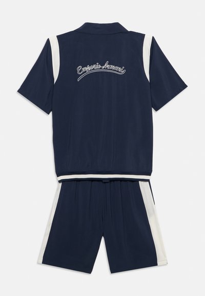 Σετ μπλε ναυτικού χρώματος με κοντομάνικο πουκάμισο και σορτς με λευκές ρίγες στο πλάι, με κεντητό λογότυπο "Emporio Armani" στην πλάτη του πουκαμίσου.