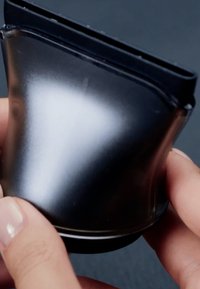 Mains tenant un appareil compact et pliable de couleur noire avec une surface lisse et réfléchissante sur un fond sombre.