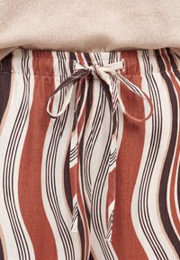 Waistband of pants with tied drawstring in brown, white, and black vertical wavy stripes, paired with beige top fabric above.
