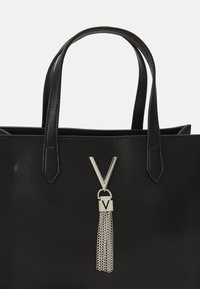 Melna struktūruota rokassoma ar divām siksnām. Iespējo sudraba "V" logotipu un ķēdes pušķa detaļu, kas piestiprināta pie slēdzenes.