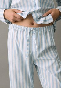 Camisa y pantalones de pijama de algodón a rayas azul claro y blancas con botones, cintura elástica y detalles de cordón ajustable.