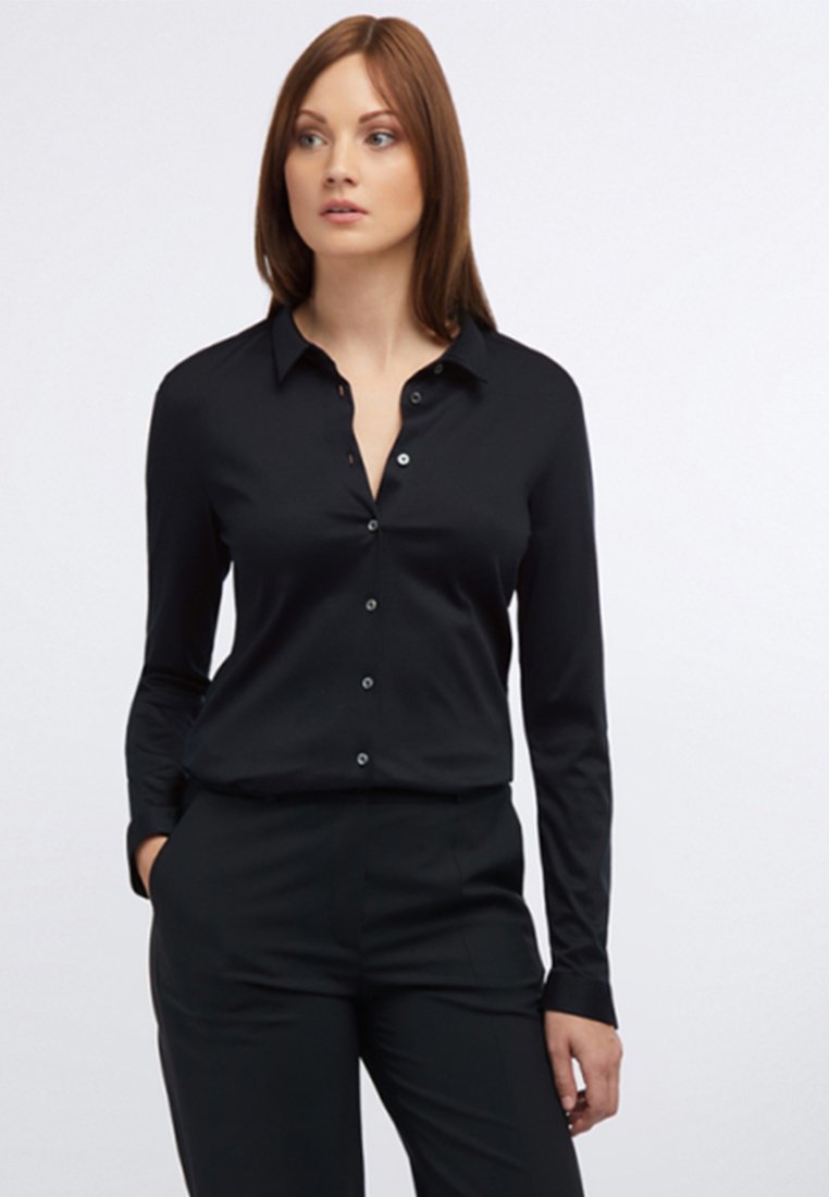 Schwarzes Langarmhemd mit Knopfleiste, Kragen und glatter Textur. Kombiniert mit schwarzen Hosen für einen stimmigen Look.