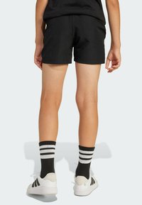 Čierne bavlnené šortky s elastickým pásom, doplnené o čierno-biele pruhované ponožky a biele tenisky s čiernymi pruhmi.