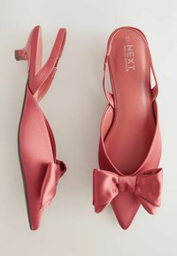 Des escarpins en satin rouge à talon slingback présentent un bout pointu et un accent en forme de nœud à l'avant. Le talon est bas et brillant. L'intérieur comporte des détails de marque.
