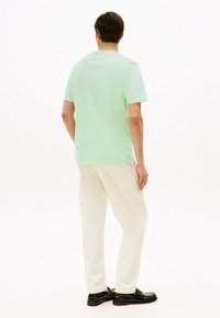 Camiseta verde menta de manga corta y corte relajado, combinada con pantalones color crema y mocasines negros, vista desde atrás.