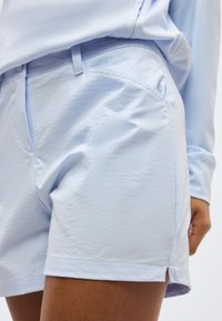 Ανοικτά γαλάζια, ραμμένα σορτς που φοριούνται με πουκάμισο σε τόνους ανοικτού γαλάζιου, μπερδεμένο μέσα, σε άτομο με μεσαίο χρωματότυπο δέρματος.