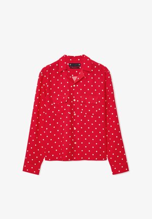 Czerwona bluzka z długim rękawem w białe kropki, zapinana z przodu, z kołnierzykiem i dwoma kieszeniami na piersi. Gładki materiał o luźnym kroju.